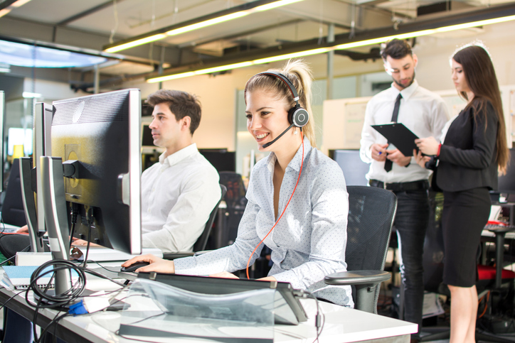 Attractive businesswoman working in call center, surrounded by colleagues.  Online support.