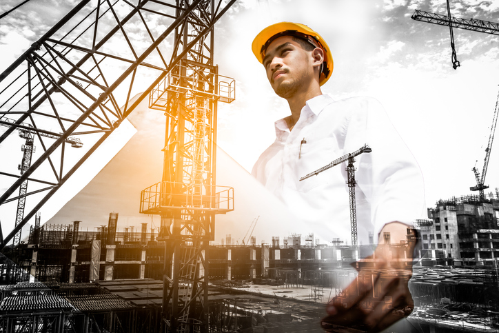 Double exposure of civil engineer holding blueprint with construction site.